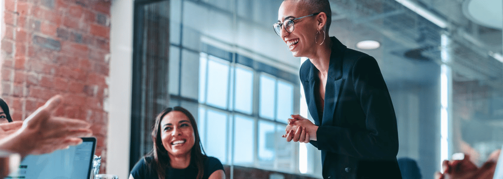 professional woman standing, smiling in office meeting with others