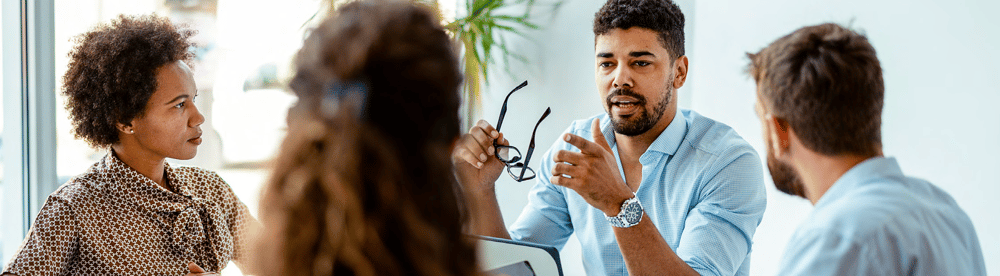 Tech man speaking in a meeting sitting down at a table Tech man speaking in a meeting sitting down at a table