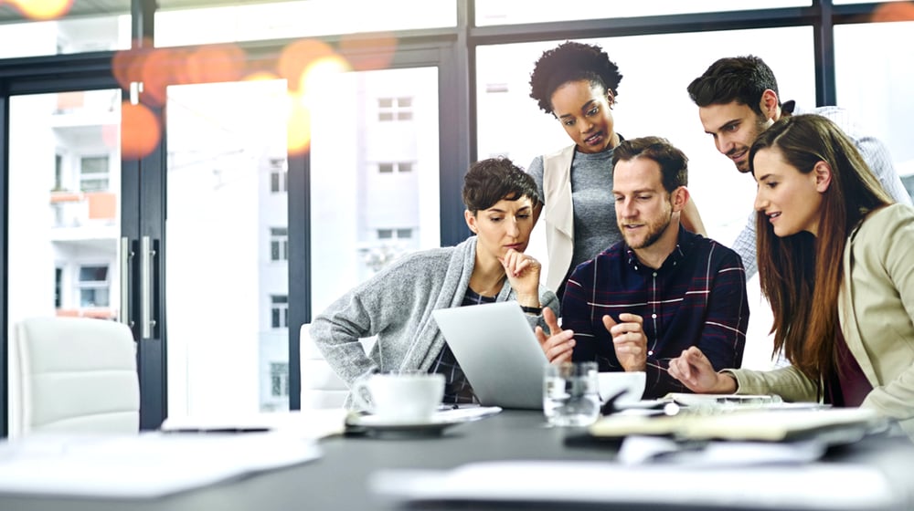multiple employees of both genders gathered around a laptop for a discussion