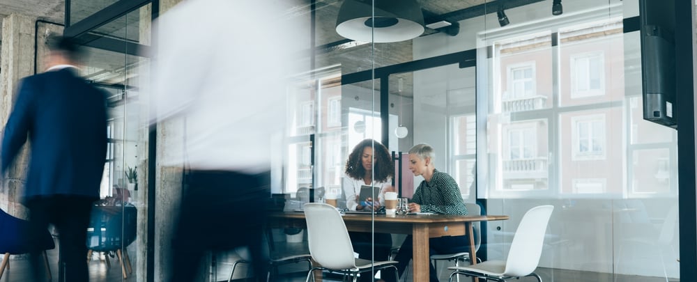 Two woman working in a clear glass conference room in an office