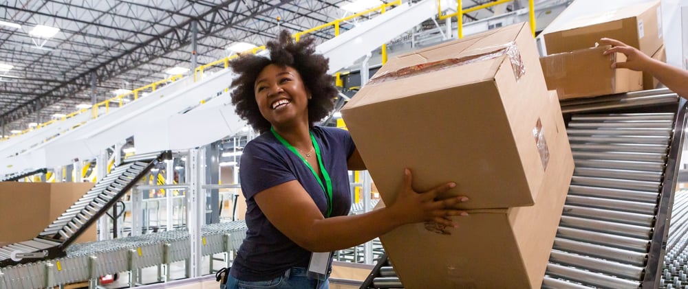 Woman smiling as she takes warehouse boxes off a conveyor Woman smiling as she takes warehouse boxes off a conveyor