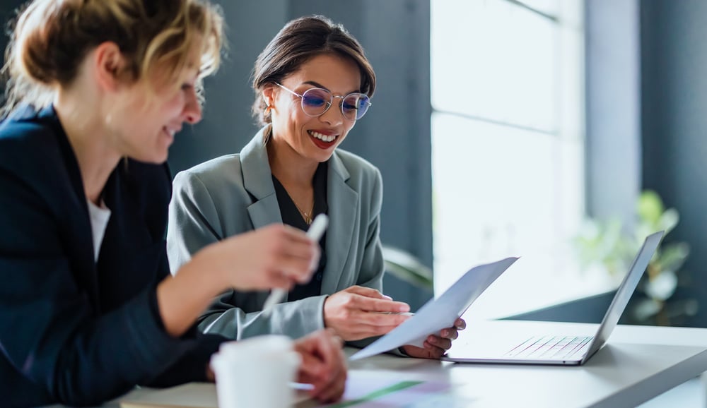 Two woman working together in an office and at a table with a laptop