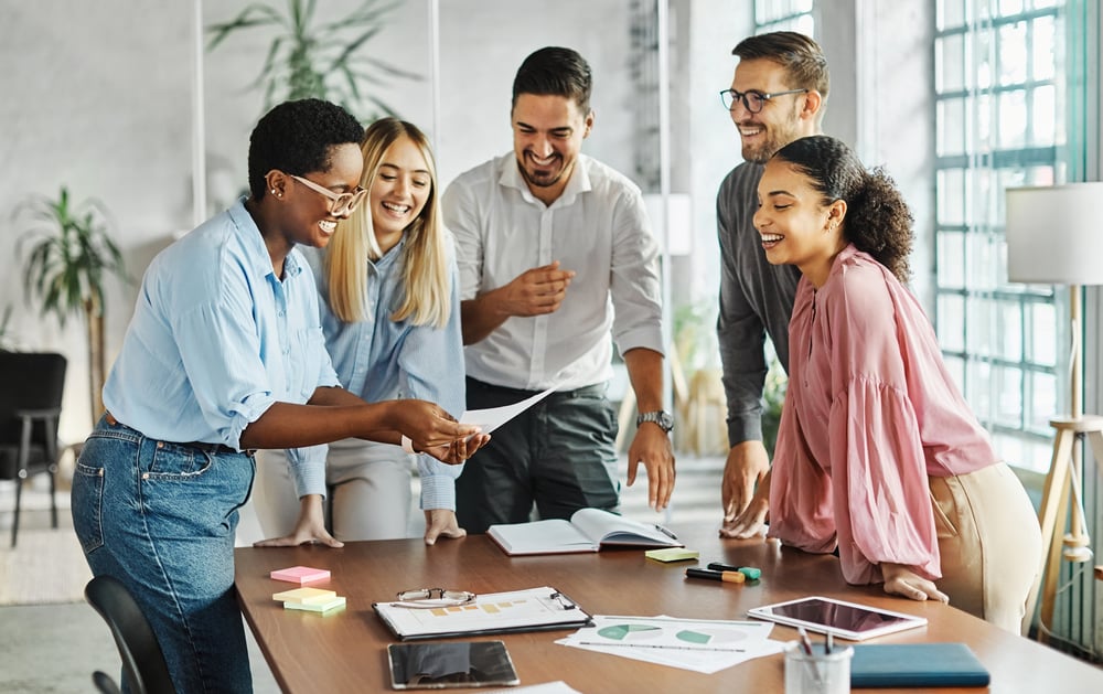 Women and men standing around a conference table in an office, smiling Women and men standing around a conference table in an office, smiling