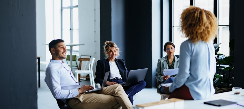Business colleagues around a table talking and on laptops