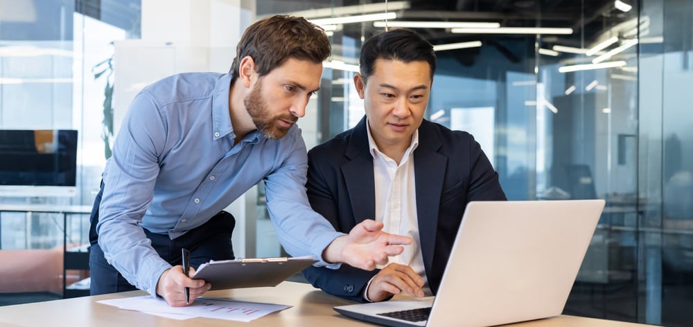 Male employee helping another male employee with his laptop work