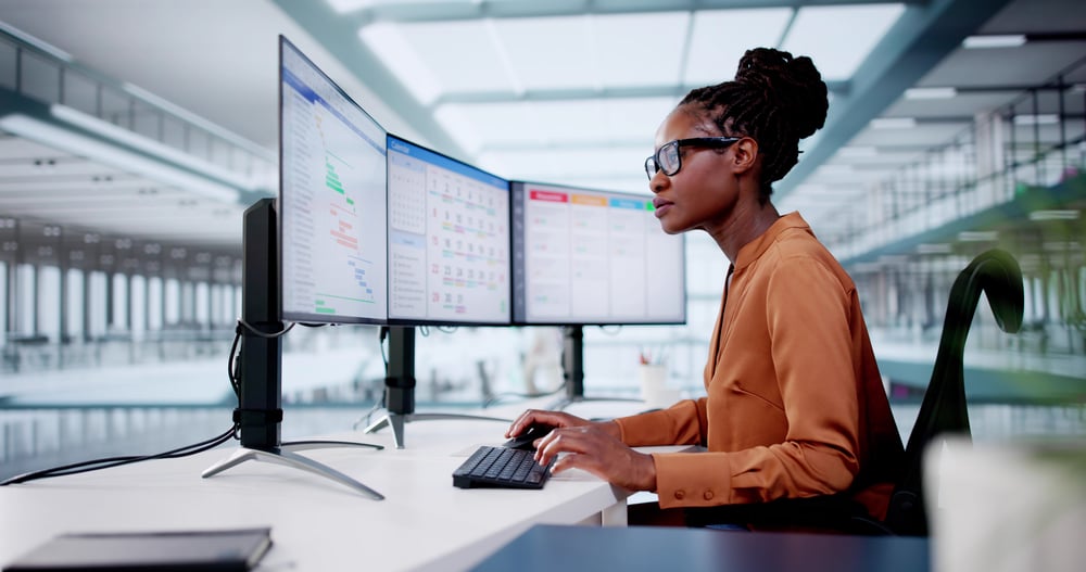A woman sitting at a desk viewing three computer monitors