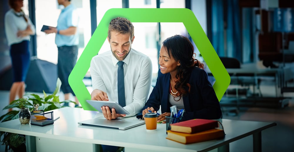 Smiling man and woman sitting at desk and working on computer tablet surrounded by a green hexagon