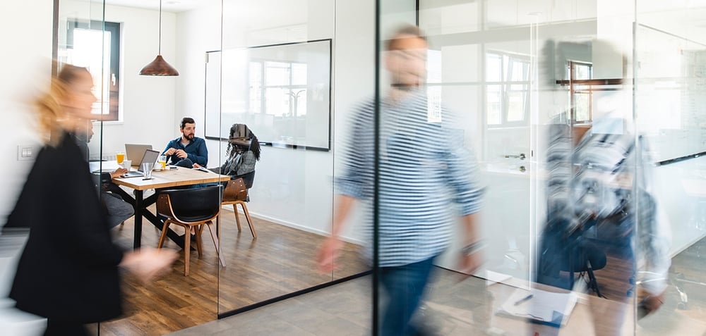 Blurred image of people walking in an office by a conference room with glass walls