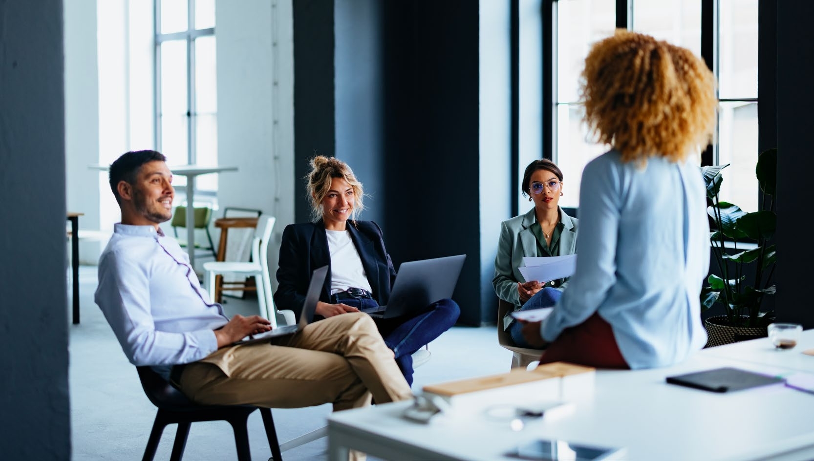 three employees sitting and facing another that is sitting on a table looking at them three employees sitting and facing another that is sitting on a table looking at them